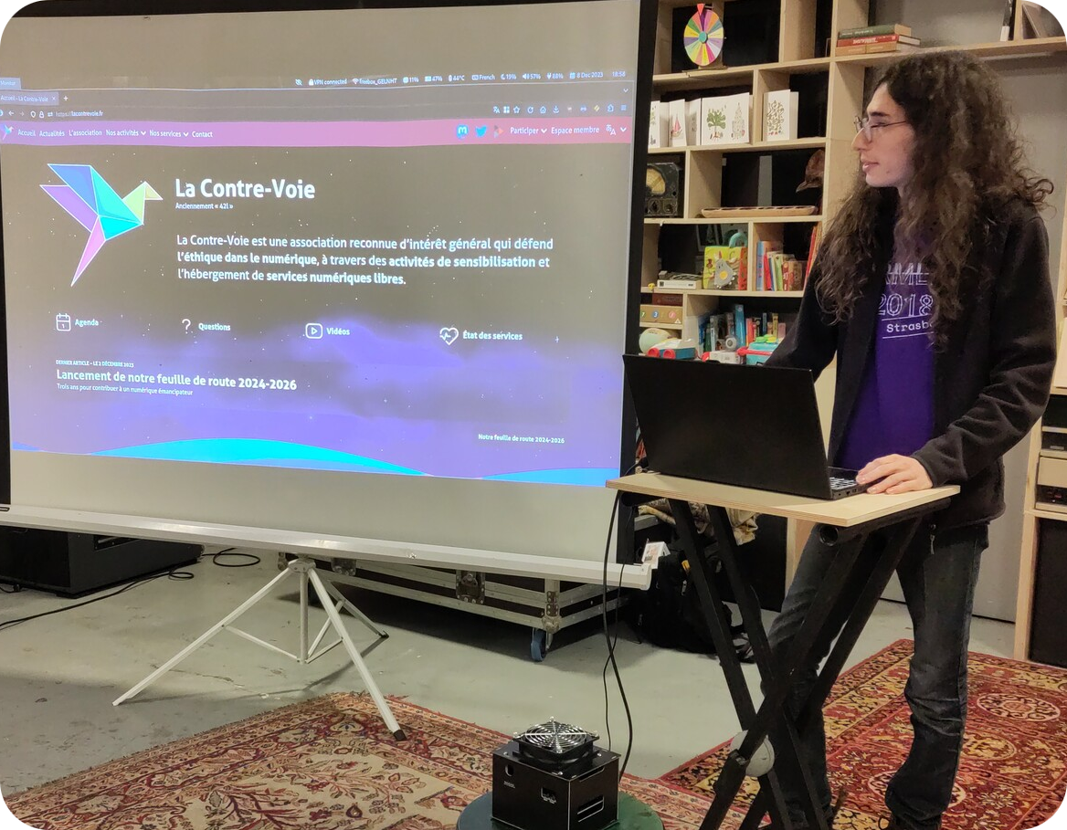 Neil debout à côté d’un vidéoprojecteur présentant le site web de l’association. Cette photo a été prise au cours d’un atelier de présentation de Nextcloud au Bêta, à la fin de l’année 2023.